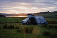 Vango Cove Air TC Inflatable Drive Away Awning Grey - Low  lifestyle image of the awning pitched in field with sunset of lake and hills in background, a couple out front having a drink