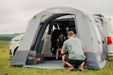 Vango Faros III Air Inflatable Drive Away Awning Cloud Grey - Low lifestyle image  front view of awning looking through to van with both front rear  doors open. Man with back to camera at the front and woman said in van floor with feet in tunnel 