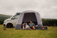 Vango Faros III Air Inflatable Drive Away Awning Cloud Grey - Low front view of awning with van behind. back door zipped up and man and woman sat in front entrance with back back