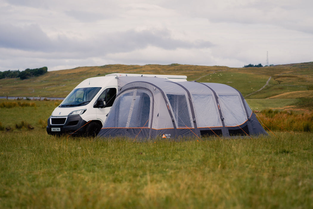 Vango Galli CC Air Inflatable Drive Away Awning - mid lifestyle image of awning attached to van with front door closed. grass field in front and hills in background