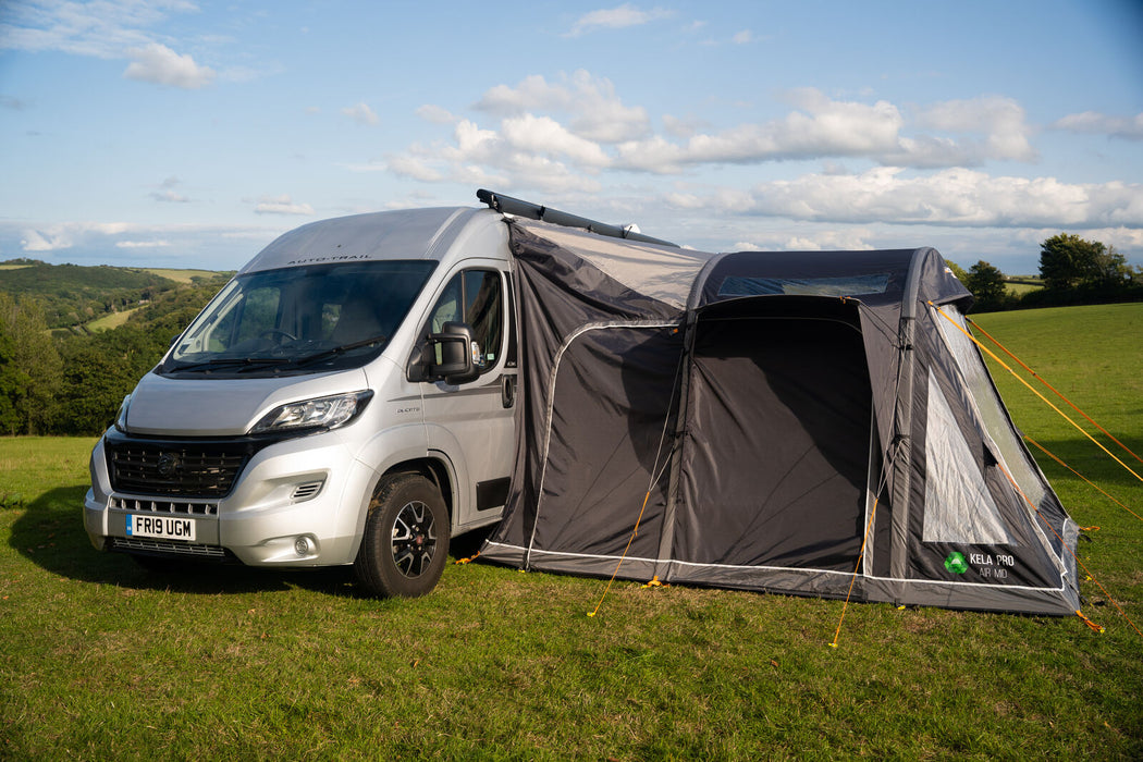 Vango Kela Pro Air Drive Away Awning - Mid lifestyle image showing left side with the doors zipped up and the front of the motorhome. pitched in field. 
