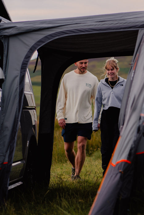 Vango Versos Air Inflatable Cloud Grey Drive Away Awning - Low lifestyle feature image of a couple walking into the tunnel from the rear of the vehicle with both doors unzipped